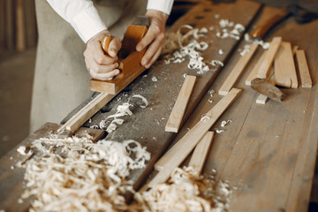 Man working with a wood. Carpenter in a white shirt. Man with a chisel