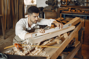 Man working with a wood. Carpenter in a white shirt. Worker measures a board