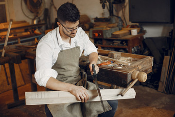 Man working with a wood. Carpenter in a white shirt. Worker with a saw