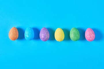 Row of many scattered colorful eggs with glitters lies on blue table on kitchen. Easter concept. Top view. Close-up