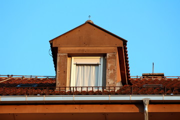 Roof window with closed white curtain and open window blinds surrounded with dilapidated insulation boards and roof tiles on top of apartment building