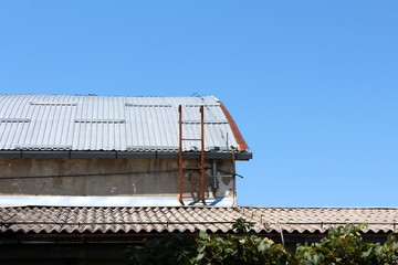 Rusted metal ladders mounted on side of abandoned dilapidated industrial complex storage hangar covered with metal roof tiles on clear blue sky background