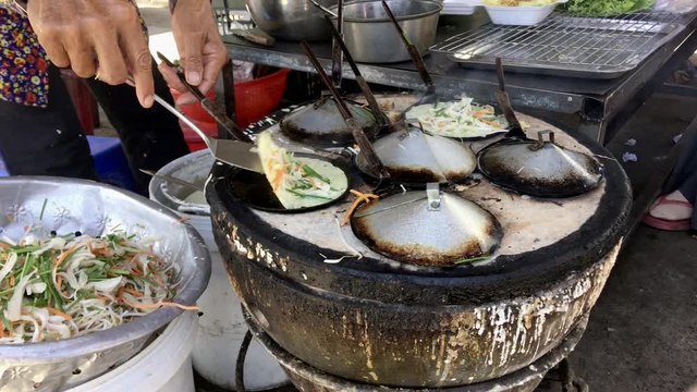 Old Vietnamese woman cooking traditional rise mini pancakes, asiatic street food.