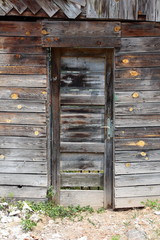Tall narrow cracked wooden boards doors mounted on abandoned suburban family house backyard entrance with grass and gravel in front