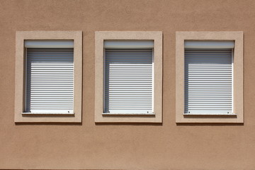 Three new suburban family house windows in a row with white plastic frames and closed window blinds surrounded with thick decorative frame of new facade