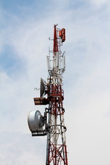 Top of strong tall cell phone red and white antenna tower with multiple antennas and transmitters on cloudy blue sky background