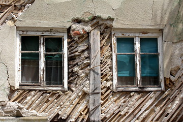 Two old windows with cracked white wooden frames on abandoned suburban family house ruins with destroyed walls in old part of town