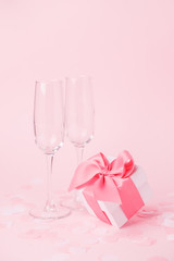 White gift box and wine glasses on pink background, decorated bow, creating romantic luxury atmosphere. For birthday, anniversary, wedding, woman day, valentine presents, gift post card