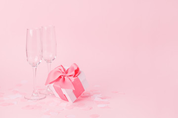 White gift box and wine glasses on pink background, decorated bow, creating romantic luxury...