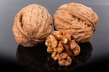 Whole walnuts and nut kernel on a dark reflective surface
