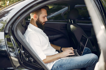 Handsome man in a white shirt. Businessman working in a car. Man use the laptop