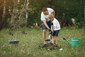 Family on a yard. Father with son planting a tree. Boy with a green funnel