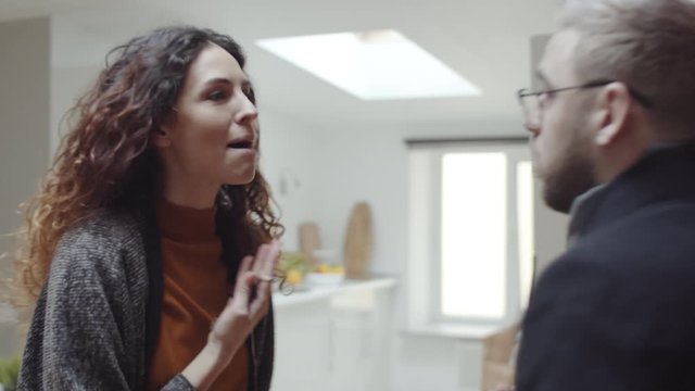 Chest-up shot of Caucasian husband and wide in coats standing face to face at home, arguing, then woman screaming, shoving man and walking away