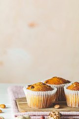 Vanilla caramel muffins in paper cups on white wooden background. Delicious cupcake with raisins, almonds and nuts. Homemade biscuit cakes. Copy space for text..