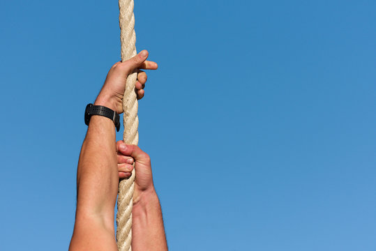 Athletic man working out and climbing a rope, during obstacle course in boot camp