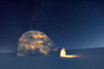 Wintry scene with snowy igloo and milky way in night sky. Fantastic winter landscape glowing by...