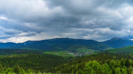 Fototapeta na wymiar Magnificent panoramic view the coniferous forest on the mighty Carpathians Mountains and beautiful sky and village background. Beauty of wild virgin Ukrainian nature. Peacefulness