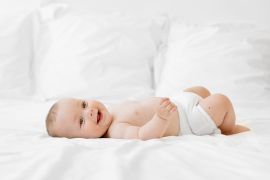 Laughing chubby baby lying on white bed