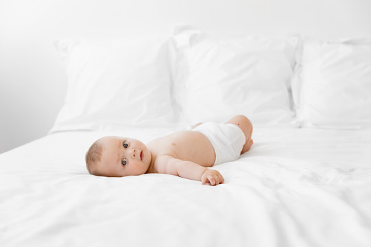 Cute baby lying on white bed looking at camera