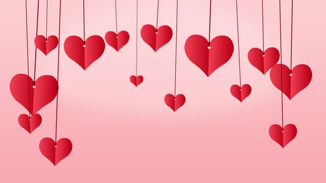 Red paper hearts hanging on red string with copy space on pink background
