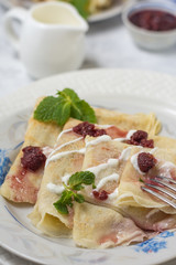 Pancakes on a plate with sour cream and raspberry jam and sprigs of mint with devices on a gray background. Vertical closeup arrangement.