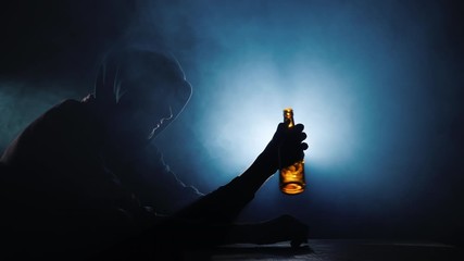Silhouette of a man sitting with an empty bottle of alcohol in his hand