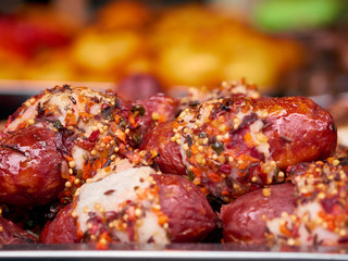 Heap of freshly grilled beef or pork meat sausages covered with spices and sauce at street food festival, selective focus, close-up. Unhealthy oily barbeque street fast food for meat lovers concept
