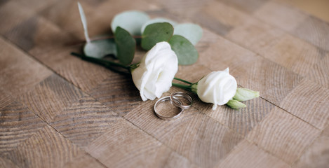 white roses and wedding rings on wooden background