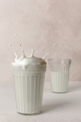 Splash of milk from a glass on a light background. Two transparent glasses with fresh milk. Dairy concept. Copy space. 
