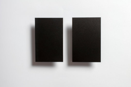 Two black blank glossy textured business cards flying and isolated over the white paper background, .UK standard size 85 mm x 55 mm, professional studio photo.