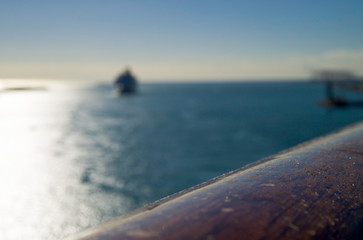 Detail of wooden railing with blurred ocean scenery and approaching cruiseship or cruise ship liner...