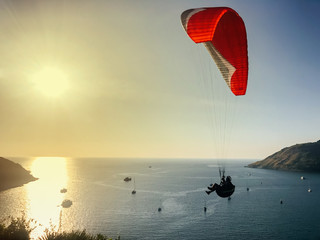 A man is engaged in paragliding. Red Parachute in the blue sky against the background of yachts, sea and islands.