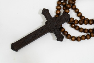 rosary beads with cross made of black wood on a white background, selected focus on christ, narrow depth of field.