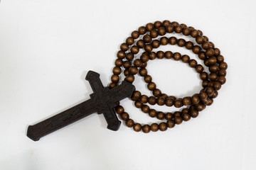 rosary beads with cross made of black wood on a white background, selected focus on christ, narrow depth of field.