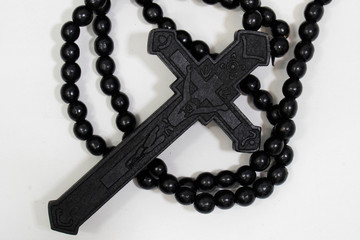 rosary beads with cross made of black wood on a white background, selected focus on christ, narrow depth of field.