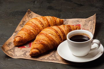 Croissants and a cup of coffee with saucer on craft paper on a dark background, vintage style