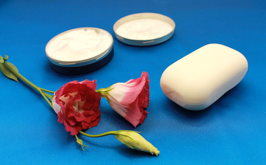 Japanese rose, natural face cream, toilet soap and body washcloth on a blue background.