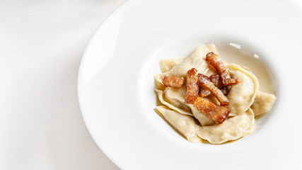 Ukrainian cuisine. vareniki with potatoes and fried pork fat - cracklings. Serving dishes in a restaurant in a white plate with sour cream. background image, copy space text
