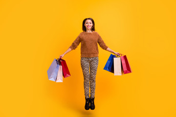 Fototapeta premium Full body photo of pretty overjoyed lady jump high carry packs addicted shopaholic wear casual fluffy sweater leopard trousers boots isolated yellow color background
