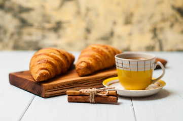 Tasty croissants and coffee in yellow cup with cinnamon on a light background