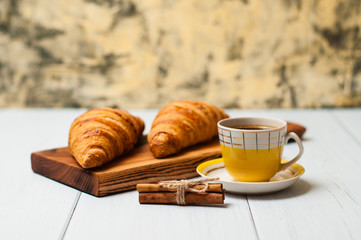 Tasty croissants and coffee in yellow cup with cinnamon on a light background