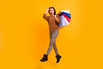 Full body profile photo of funny shocked lady jump high carry packs shopaholic open mouth new sales wear fluffy sweater leopard trousers boots isolated yellow color background