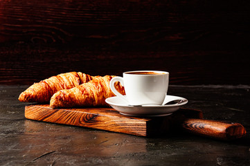 Concept of delicious breakfast, croissants and espresso on dark wooden board.