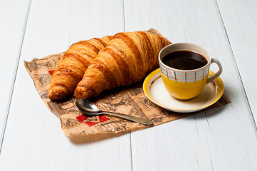 Espresso coffee in vintage yellow cup with a saucer and spoon, croissants on craft paper, on a light background, breakfast concept