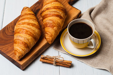 Coffee in vintage yellow cup and saucer and croissants on a wooden plate, linen napkin, on light background, a rustic breakfast concept
