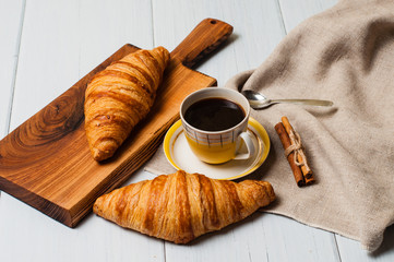 Coffee in a vintage yellow cup with a saucer, spoon and croissants with cinnamon on wooden plate, linen napkin, on a light background, a rustic breakfast concept
