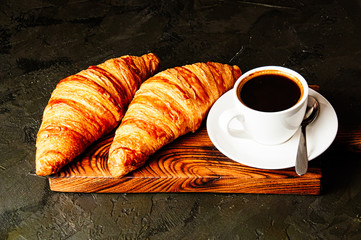 Concept of delicious breakfast, croissants and espresso on dark wooden board.