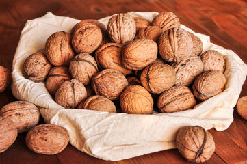 Whole walnuts on rustic old wooden table, walnuts in a reusable cloth bag