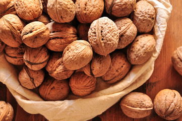 Whole walnuts on rustic old wooden table, walnuts in a reusable cloth bag