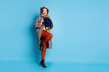 Full length profile photo of amazing lady jumping high up holding stylish retro cap wear casual long grey coat scarf trousers shoes isolated blue color background